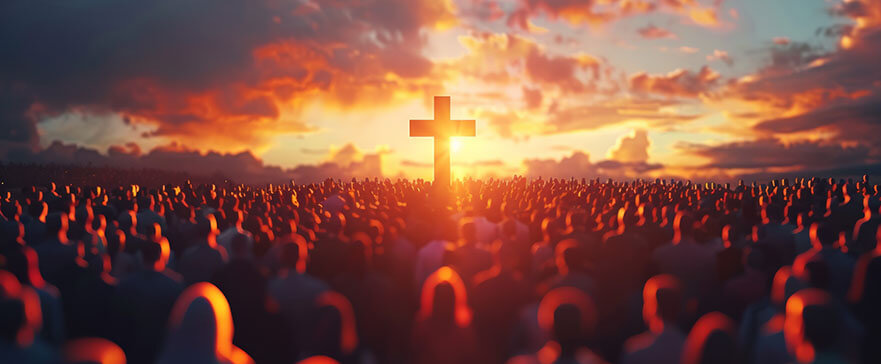 A large crowd gathered at sunrise facing a glowing cross in the